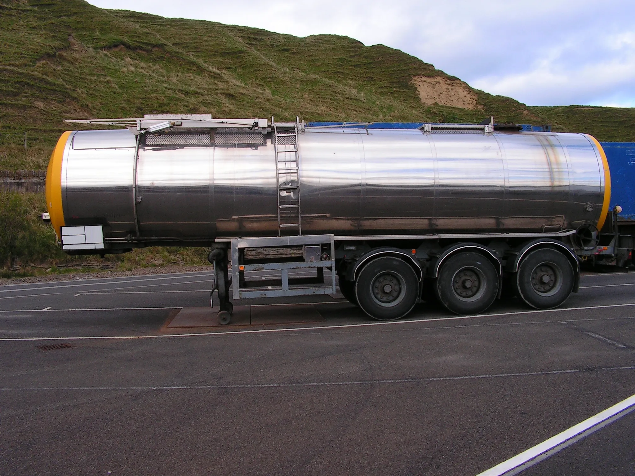 Shiny tanker truck on road with green hills background.